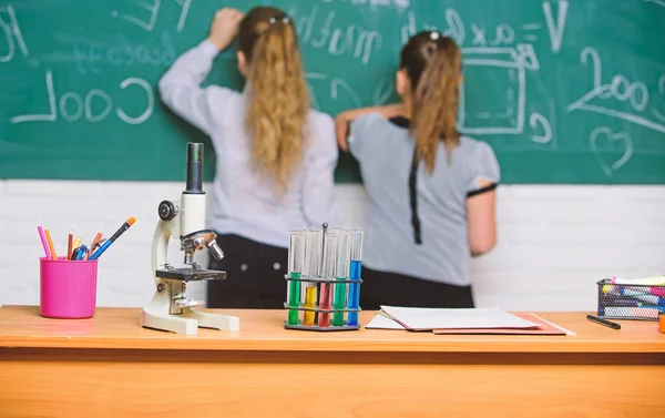 Дівчата однокласники вивчають хімію. Мікроскоп і пробірки на столі. Хімічні реакції. Зробити вивчення хімії цікавим. Учень на шкільній дошці на уроці хімії. Концепція освітнього експерименту — стокове фото