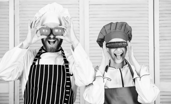 Healthy happy diet. Master cook and helper playing with vegetables in kitchen. Chef and kitchen maid holding tomatoes and cucumber at eyes. Couple of cooks having fun with natural food in restaurant