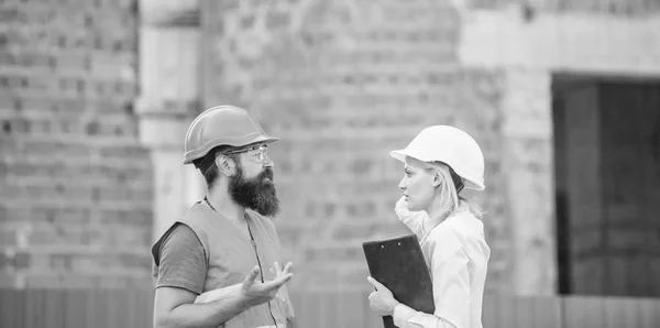 Safety inspector concept. Construction site safety inspection. Discuss progress project. Woman inspector and bearded brutal builder discuss construction progress. Construction project inspecting