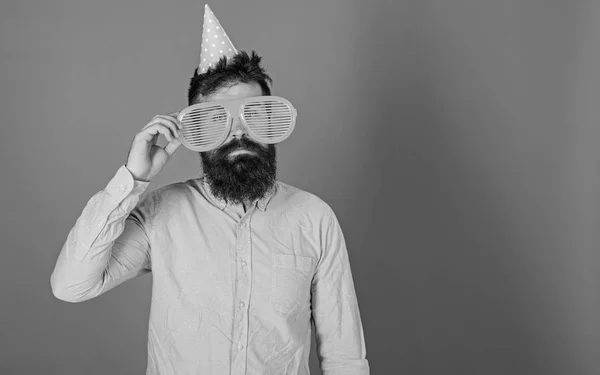 Homem com barba e bigode no rosto calmo solitário em seu aniversário, fundo azul. O tipo de chapéu de festa celebra sozinho. Conceito de aniversário. Hipster em óculos de sol gigantes celebrando aniversário, espaço de cópia — Fotografia de Stock