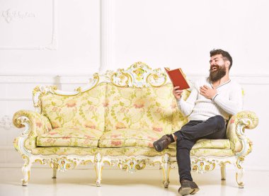 Adam zevk ile eski kitap okuma. Sakal ve bıyık oturur barok tarzı kanepe, tutar kitap, beyaz duvar arka plan üzerinde olan adam. Maço üzerinde yüz kitap okuma gülüyor. Mizahi edebiyat kavramı