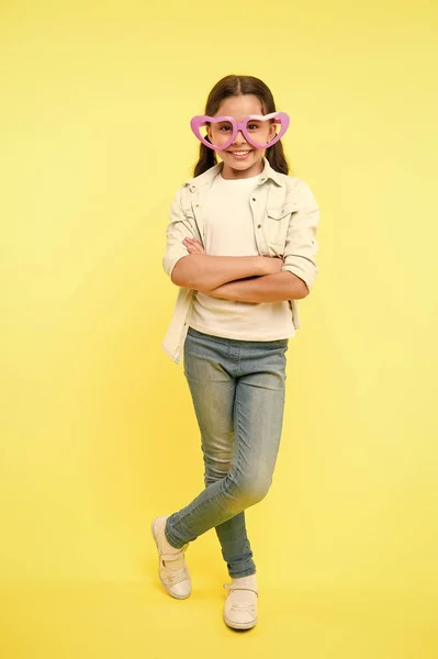 Дитячі окуляри у формі серця виглядають впевнено. Дівчина носить милі окуляри впевнене обличчя. Дитина впевнена, що весела позує складеними руками. Вона знає, як залишатися позитивним у будь-якій ситуації. Впевнена поза — стокове фото
