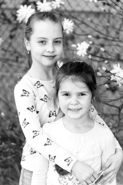 Små flickor poserar på blommor i vårträdgården. Systrar njuter av vårdagen utomhus. Barn med blommande blommor. Familj, kärlek och tillit — Stockfoto