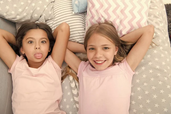 Bästa vänner för evigt. Flickor barn låg på sängen med söta kuddar ovanifrån. Pyjamas party konceptet. Flickor i lekfulla humör med grimas ansikte. Vänner barn att ha roligt tillsammans och känna sig bekväma — Stockfoto