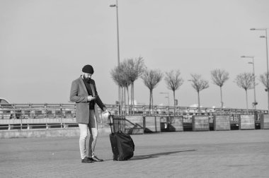 Bavullu gezgin havaalanı tren istasyonuna gitmek için bekliyor. Yola çıkmaya hazırız. Seyahat çantası taşı. İş gezisi. Tekerlekli bavul taşıyan sakallı bir hippi. Yolculuk başlasın.