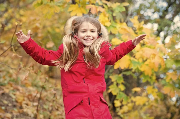 Comodo e spensierato. Capelli lunghi biondi bambino che camminano in giacca calda all'aperto. Ragazza felice in cappotto rosso godere di autunno parco naturale. Bambino indossare cappotto alla moda con cappuccio. Autunno vestiti e concetto di moda — Foto Stock