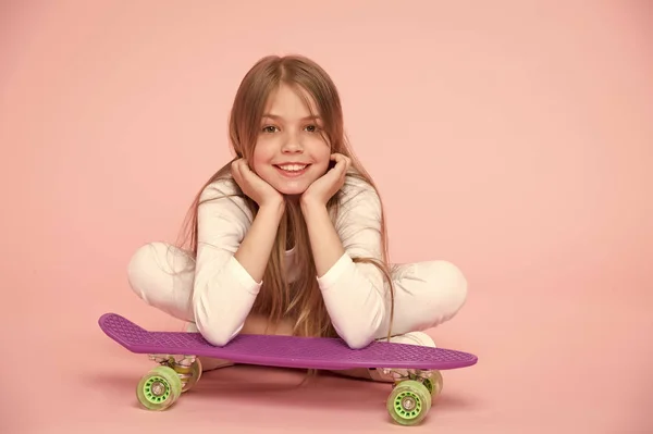 Miúdo de skate deitado no chão sobre fundo rosa. Criança patinadora sorrindo com longboard. Menina pequena sorriso com skate bordo. Estilo de vida infantil e jogos ativos. Atividades esportivas e energia, pastel punchy — Fotografia de Stock