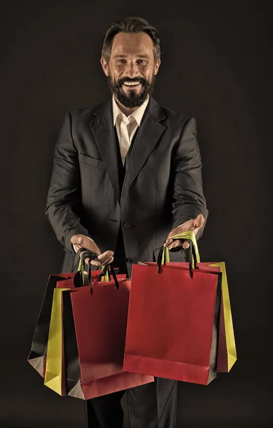 Happy to share. Man mature shopper carries shopping bags black background. Successful businessman choose only luxurious brands and shopping in high fashioned boutiques. Gifts for colleagues