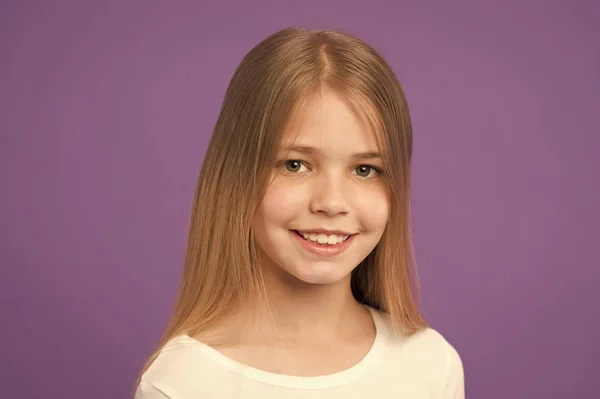 Menina no rosto sorridente com cabelos longos usa camisa branca, fundo violeta. Menina gosta de olhar bonito, elegante e elegante. Miúda com cabelo comprido parece adorável. Penteado e conceito de cuidado do cabelo — Fotografia de Stock