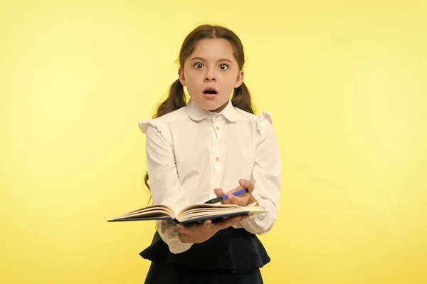 Girl cute schoolgirl in uniform hold book with information yellow background. Pupil get information from book. Child wear school uniform prepare for lesson information. Surprised about information — Stock Photo, Image