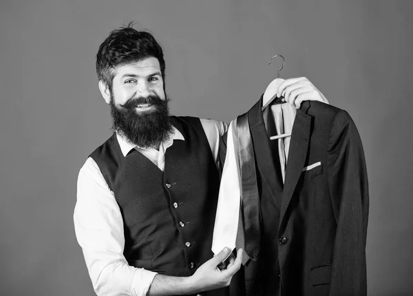 Shop assistant or personal stylist service. Matching necktie outfit. Man bearded hipster hold neckties and formal suit. Perfect necktie. Shopping concept. Stylist advice. Difficulty choosing necktie