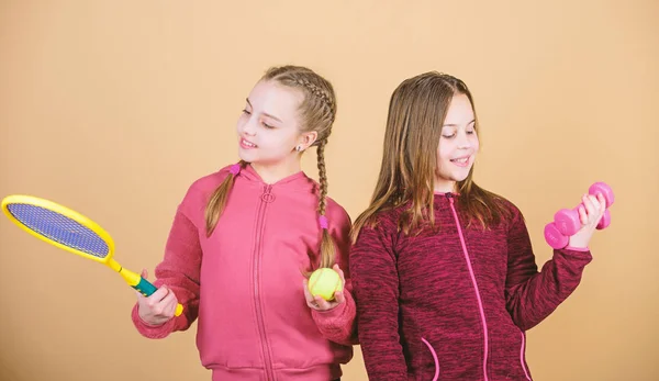 朋友们准备好训练了帮助孩子们找到自己喜欢的运动的方法。女孩可爱的孩子与运动器材哑铃和网球拍。我们喜欢运动。孩子可能擅长完全不同的运动 — 图库照片