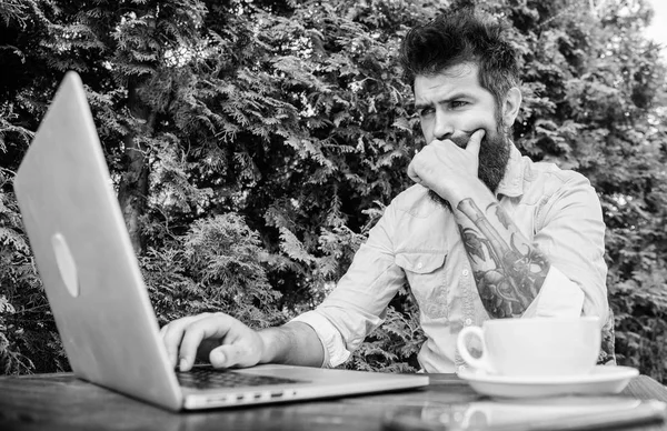 Watching blog for more information. Bearded man writing new blog post in summer cafe. Blogger keeping private blog. Hipster posting on online social network or blog on natural landscape