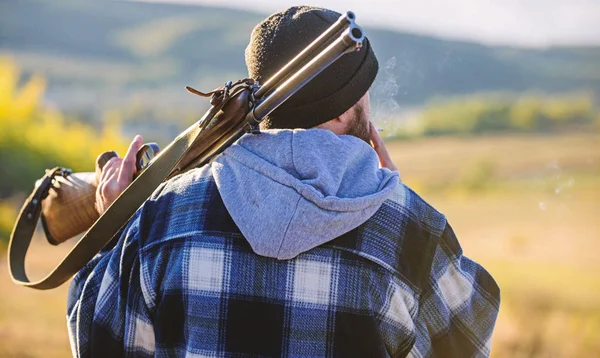 Brutalità e mascolinità. Hunter portare pistola da fucile sulla spalla vista posteriore. Un cacciatore di uomini passa il tempo libero a caccia. Caccia maschile hobby concetto di svago. Uomo brutale ragazzo guardiacaccia in cappello natura sfondo — Foto Stock