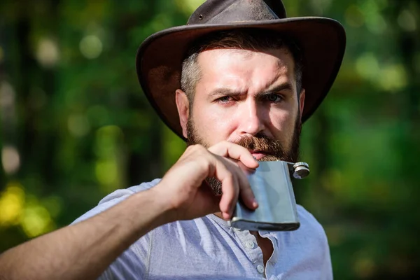 Calentando el salvaje oeste. Primavera tiempo soleado. camping y senderismo. macho maduro con aspecto brutal beber alcohol del frasco. Hombre barbudo con sombrero de vaquero en el parque al aire libre. hombre hipster en otoño bosque —  Fotos de Stock