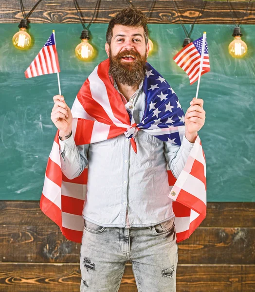 Professora americana acena com bandeiras americanas. Programa de intercâmbio de estudantes. Conceito de educação patriótica. Homem com barba e bigode no rosto feliz segura bandeiras dos EUA, em sala de aula, quadro-negro no fundo — Fotografia de Stock