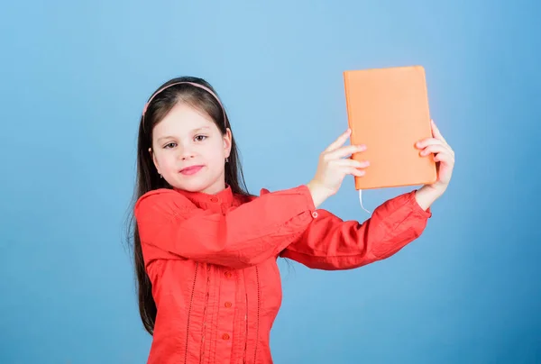 Mira este libro. Un pequeño alumno tomó el libro de la biblioteca. Niño adorable de la escuela con libro de actividades. Linda niña sosteniendo el cuaderno con cubierta naranja, espacio para copiar —  Fotos de Stock