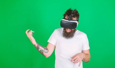 VR gözlüklü adam gitar çalmayı öğreniyor. Hipster gitarist hevesli bir yüz üzerinde modern teknolojiyi eğlence için kullanır. Gözlüklü, yeşil arka planda sakallı bir adam. VR müzisyen konsepti