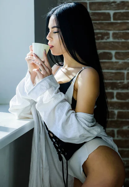 Seksi göğüslü seksi kız pencere kenarında kahve içiyor. Çekici kadın iç çamaşırları evde dinleniyor. Tutkulu gizemli aşık. Kahve zamanı. Ama önce kahve. Sabah güneşinin tadını çıkarıyorum.