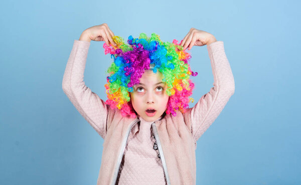 Playing with her hair. Funny kid with curly synthetic hair. Cute little girl with fancy hair. Adorable small child wearing bright clown hair wig