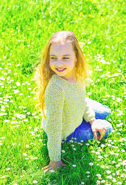 Kız grassplot, arka planı yeşil çimlere oturur. Altın Çağ kavramı. Yüz gülümseyerek kıza harcamak açık havada eğlence. Çocuk çayır otururken bahar güneşli hava keyfini çıkarın