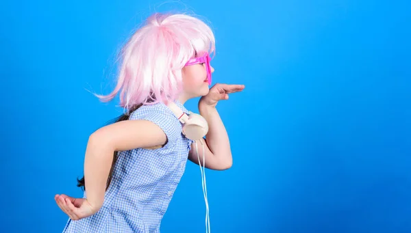 Inspired by music. Little kid listening music. Cute kid with headphones blue background. Small girl headphones pink wig dancing. Child using technology for fun. Modern headphones. Energy motion dance