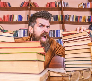 Öğretmen ya da öğrenci sakallı defocused gözlük ile masada oturur. Çılgın bilim adamı kavramı. Yüz Kitaplığı'nda, eğitim sırasında kitaplar, kitap rafı arka plan üzerinde yığınları arasında bağıran adamın