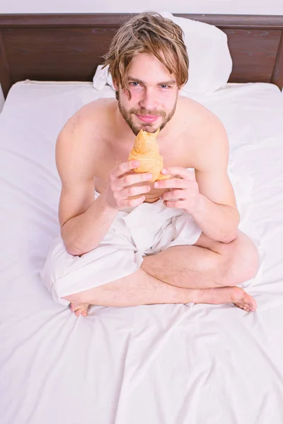 Свіжі хлібобулочні продукту. Людина бородатий красивий хлопець їжі сніданок в ліжко. Французький сніданок стереотип. Хлопець тримає круасан sit ліжку в спальні номер або hotel. Людина їсть круасани, він любить хлібобулочних виробів — стокове фото