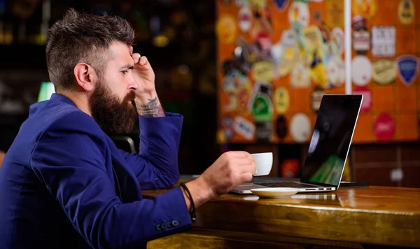 Surfing internet. Freelance benefit. Man bearded businessman sit pub with laptop and cup of coffee. Manager work online while enjoy coffee. Online job. Hipster freelancer work online blog notebook