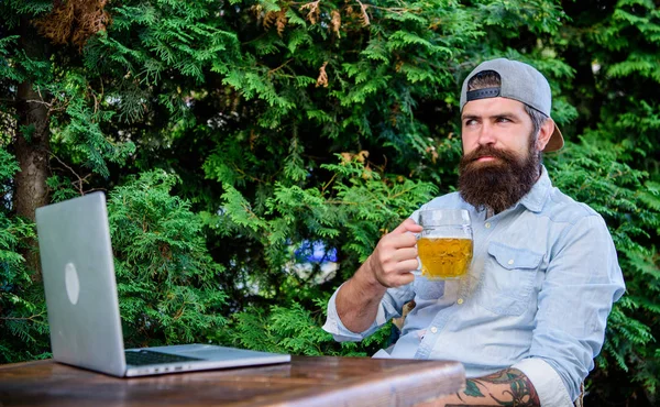 Brute Man Leisure met bier en online spel. Eindelijk vrijdag. Hipster ontspannen zitten terras buiten met bier. Bearded hipster freelancer geniet van einde werkdag met Bierpul. Hij verdient deze pint — Stockfoto