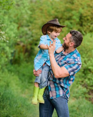 Eko çiftliği. Küçük çocuk çiftçilikte babasına yardım ediyor. Baba oğul çiftlikte kovboy şapkası takıyor. Lastik çizmeli çocuk. Ormanda mutlu bir baba. İnsan ve doğa. Aile günü. Dünya günün kutlu olsun. Mutlu aile