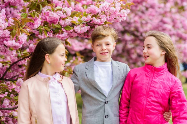 I bambini godono della calda primavera. Perso in fiore. Ragazze e ragazzi che posano vicino a Sakura. Bambini su fiori rosa di sfondo albero di sakura. Ai bambini piace il sakura ai fiori di ciliegio. Buone vacanze primaverili — Foto Stock