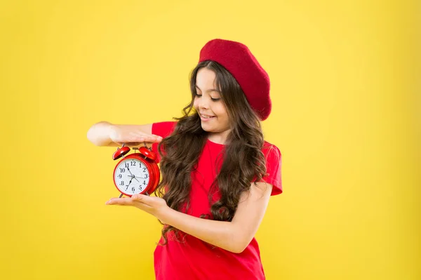 Menina feliz com cabelos longos encaracolados na boina. criança com despertador. Moda intemporal. criança parisiense em amarelo. Cabeleireiro de beleza. menina em chapéu de estilo francês. Menina mostra o tempo no relógio — Fotografia de Stock