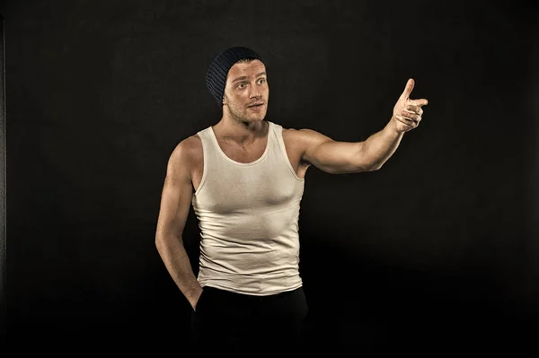 Trainer point finger on dark background. Man in trendy vest and hat. Athlete with bristle on serious face. Training and workout. Fashion style and trend, vintage filter