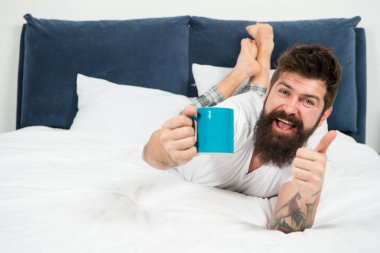 Taze kahvenin tadını çıkarıyorum. mutlu sakallı adam hipster içmek sabah kahve. yatak odasında acımasız uykulu adam. yatakta pijama sakallı olgun erkek. uykuda ve uyanık. enerji ve yorgunluk. Taze kahve