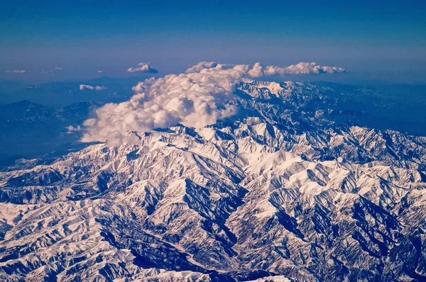Montañas cubiertas de nieve y nubes, vista aérea. Superficie del planeta Tierra. Viajando alrededor del mundo. Protección del medio ambiente y ecología. Tomo mi tierra con un poco de cielo azul —  Fotos de Stock