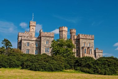 Lews Castle on blue sky in Stornoway, United Kingdom. Castle with green trees on natural landscape. Victorian style architecture and design. Landmark and attraction. Summer vacation and wanderlust clipart