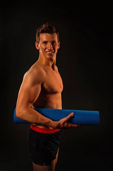 Sportman glimlach met yoga mat. Atleet glimlachend met sexy lichaam en borst. Gelukkig man met gespierde armen met de biceps. Fitnessapparatuur voor opleiding en training. Sport activiteit van yoga en Pilatesoefeningen — Stockfoto