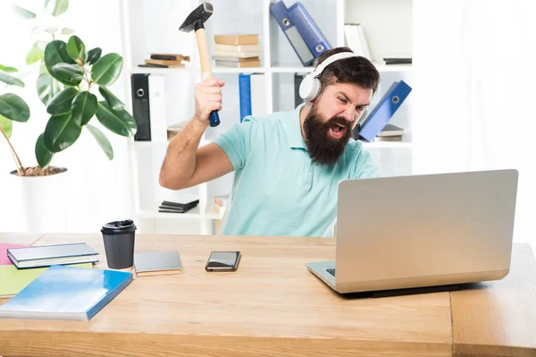 Man bearded guy headphones office swing hammer on computer. Slow internet connection. Outdated software. Computer lag. Reasons for computer lagging. How fix slow lagging system. Hate office routine
