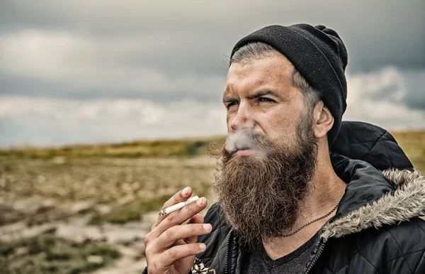 Man met baard roken sigaret bij mountain, bewolkte hemel — Stockfoto