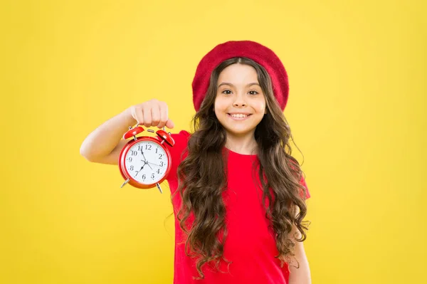 Winkelen, verkoop en tijd concept. Parijse kind op geel. kind met wekker. Tijdloze mode. gelukkig meisje met lang krullend haar in baret. Schoonheidskapster. klein meisje in franse stijl hoed — Stockfoto