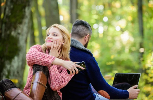 couple in love relax in autumn forest with phone and laptop. happy girl dreaming outdoor. man sit with back. Spring mood. camping and hiking. Family picnic. Relationship. Full concentration at work