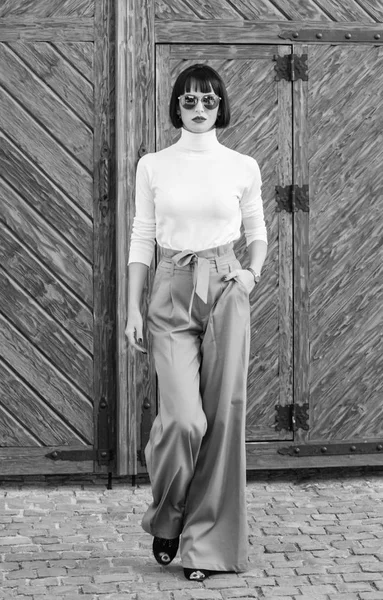 Fashionable outfit slim tall lady. Fashion and style concept. Woman walk in loose pants. Woman fashionable brunette stand outdoors wooden background. Girl with makeup posing in fashionable clothes