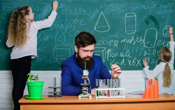 Durante la clase. Profesora y alumnas en clase de laboratorio. Hombre barbudo enseñando química. Los niños pequeños de la escuela que recitan lección en clase de ciencias — Foto de Stock