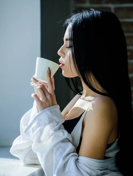 Drinking alone. Pretty woman drinking fresh hot coffee at window. Sensual girl drinking her favorite morning beverage. Sexy girl holding ceramic drinking cup