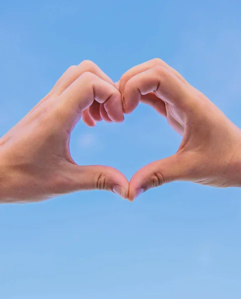 Händer satt ihop i hjärtat formen blå himmel bakgrund. Love symbol koncept. Hand hjärtat gest bildar formen med fingrarna. Manliga händer i hjärtat formen gest symbol för kärlek och romantik — Stockfoto