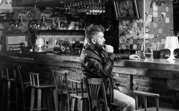 Hipster relajarse en el bar con cerveza. Hombre con barba pasar el ocio en el bar oscuro. Brutal hombre barbudo hipster sentarse en el mostrador del bar beber cerveza. Viernes por la noche. Bar es un lugar relajante para tomar una copa y relajarse — Foto de Stock