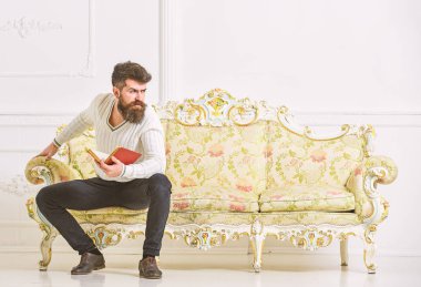 Sakal ve bıyık oturur barok tarzı kanepe, tutar kitap, beyaz duvar arka plan üzerinde olan adam. Maço katı yüz kitap okumayı yeni bitirdim. Edebiyat kavramı üzerine düşünceler. Adam edebiyat hakkında düşünme