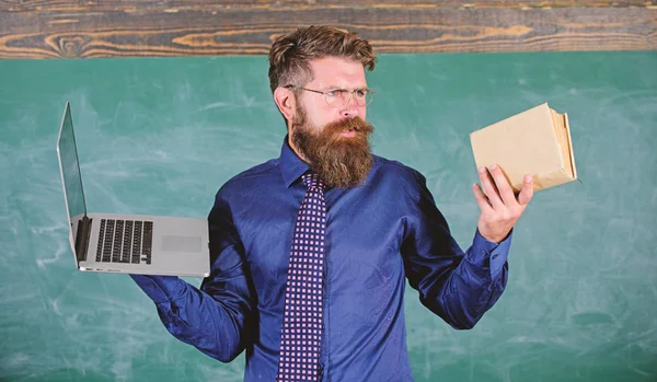 Professeur hipster barbu tient livre et ordinateur portable. Choisissez la bonne méthode d'enseignement. Enseignant choisissant une approche pédagogique moderne. Les technologies modernes en bénéficient. Moderne à la place dépassé. Numérique contre papier — Photo