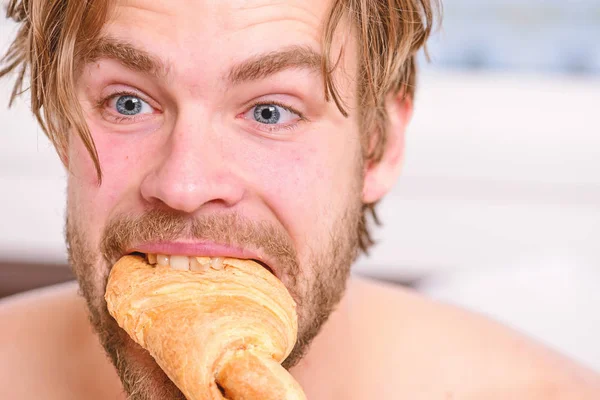 Bell'uomo che naviga in internet a letto. Bachelor si diverte. Giovane uomo di felicità sul letto con godersi la vacanza e la mattina tazza di caffè e croissant. Colazione francese . — Foto Stock